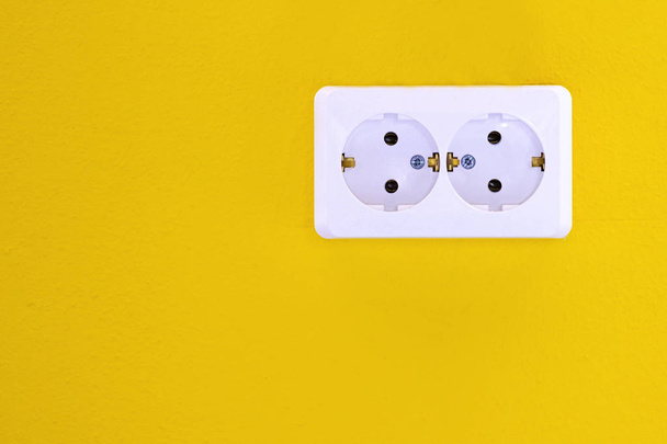 Pusty, odłączony Europejski gniazdka elektrycznego z bliska na żółtym tle. Białe gniazdo elektryczne na żółtej ścianie. Zbliżenie - Zdjęcie, obraz