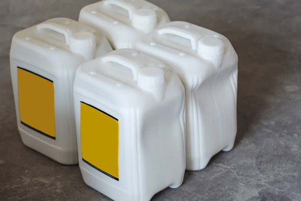 embalaje blanco de plástico galones en blanco con una tapa blanca y una etiqueta en blanco amarillo sobre un fondo gris
 - Foto, imagen
