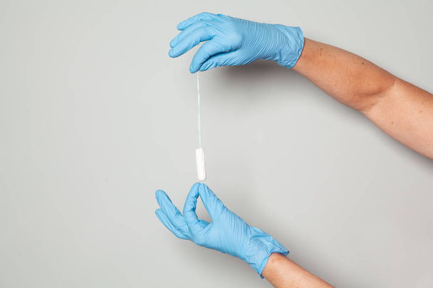 Age woman hand in medicine glove holding tale of hygienic tampon on grey background. - Photo, Image
