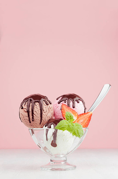 Delicious classic different color ice cream scoops in  bowl with mint, spoon, chocolate sauce, strawberry slices in pink interior on white wood board, vertical. - Foto, afbeelding