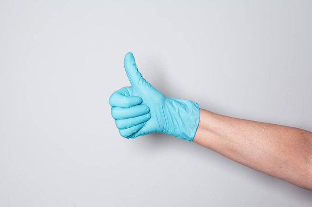 Hand in blauwe siliconen handschoen op grijze achtergrond toont het teken OK. - Foto, afbeelding