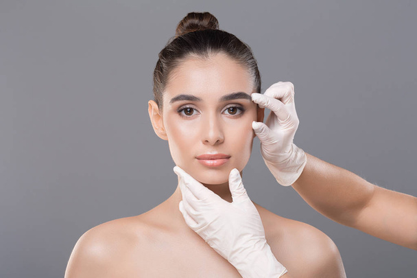 Kosmetikerin mit Handschuhen untersucht Frauengesicht - Foto, Bild