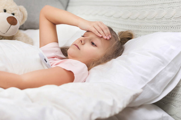Sick little girl lying in bed with thermometer - Foto, Imagem