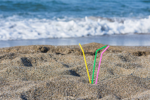 Plastic colored straws tubules for drinking in the sand on the beach. Concept - Photo, image