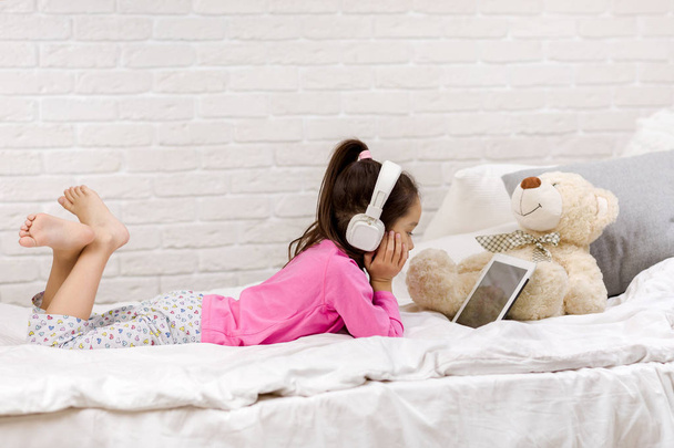 cute little girl lies in bed uses digital tablet. - Foto, Imagen