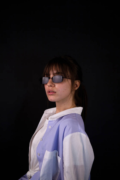 Beyaz gömlekli beyaz kız, siyah güneş gözlüğü ile stüdyoda poz - Fotoğraf, Görsel