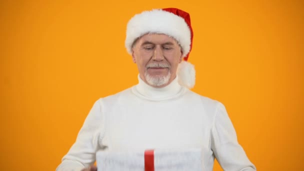 Pleased senior male in santa hat hugging giftbox, rejoicing new years surprise - Felvétel, videó