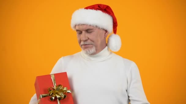 Sonriente jubilado masculino en sombrero de Santa Claus señalando con el dedo a la caja de regalo roja, descuento
 - Metraje, vídeo