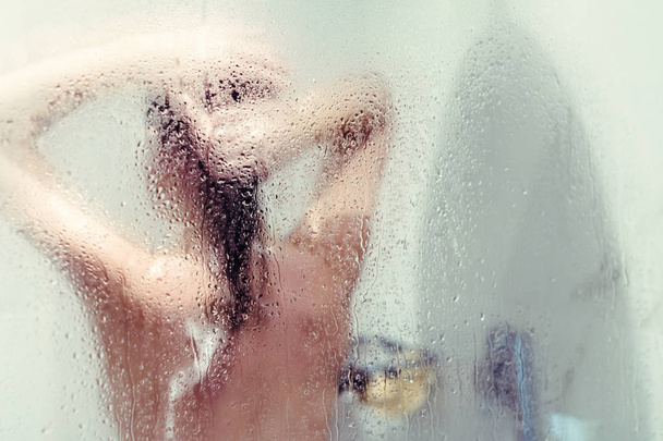 Silhouette of naked beautiful woman washing hair in shower behind wet misted glass. - Fotó, kép