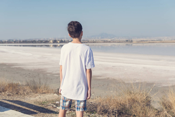 A boy in shorts and a T-shirt near the salt lake in Larnaca. Cyprus - 写真・画像