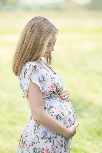 Beautiful pregnant woman in white summer dress in meadow full of yellow blooming flovers. - Zdjęcie, obraz