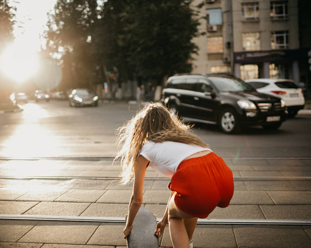 Beautiful skater woman wearing red shorts riding on her longboar - 写真・画像