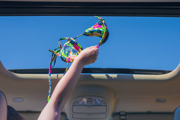 girl trowing away her bikini bra out from open hatch of a vehicle. Travel lifestyle concept - Foto, immagini