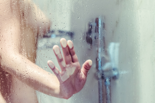 Naked beautiful woman taking a shower behind wet misted glass. - Photo, Image
