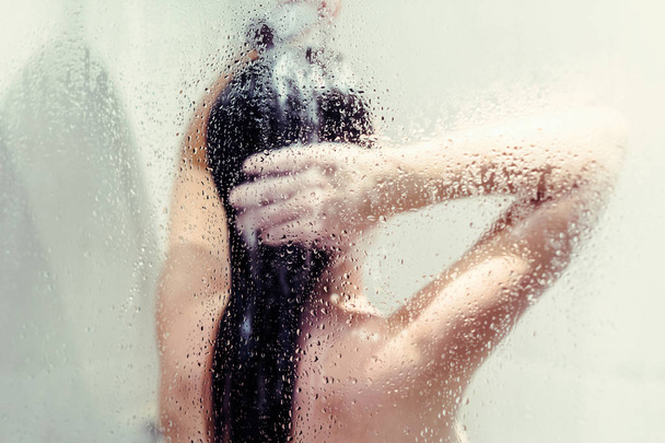 Silhouette of naked beautiful woman washing hair in shower behind wet misted glass. - Fotoğraf, Görsel
