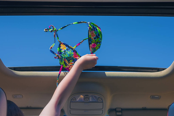 girl trowing away her bikini bra out from open hatch of a vehicle. Travel lifestyle concept - 写真・画像