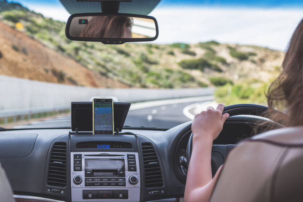 Young woman is driving on the highway in Italy and using gps navigation app on the mobile phone. View from the back seat of the car - Zdjęcie, obraz
