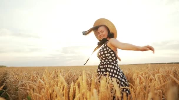 Retro dressed girl in straw hat and black dress spinning around in wheat field during sunset. Joyful, cheerful, happy woman. - Video, Çekim