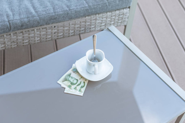 Chinesischer Yuan und leere Tasse Kaffee auf einem Glastisch eines Cafés im Freien. Bezahlung, Trinkgeld. - Foto, Bild