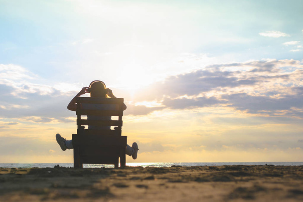 Girl in headphones is sitting on the sun lounger listening to music on the beach at sunset. Summer concept. - Valokuva, kuva