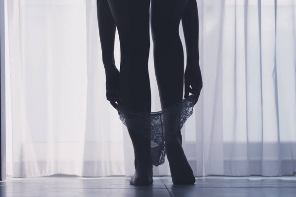 Alulnézet sziluettje gyönyörű nő, szexi lábak levette fehér bugyi egy szobában háttérben a függöny - Fotó, kép
