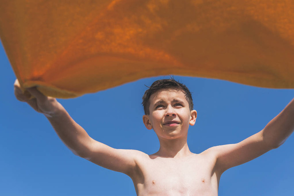 Bottom view on the boy with yellow towel on the blue sky background. Concept. - Zdjęcie, obraz