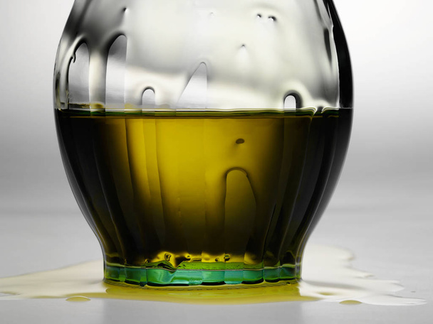 Warme gele groene gloed door rommelig olijfolie fles met druppels - Foto, afbeelding