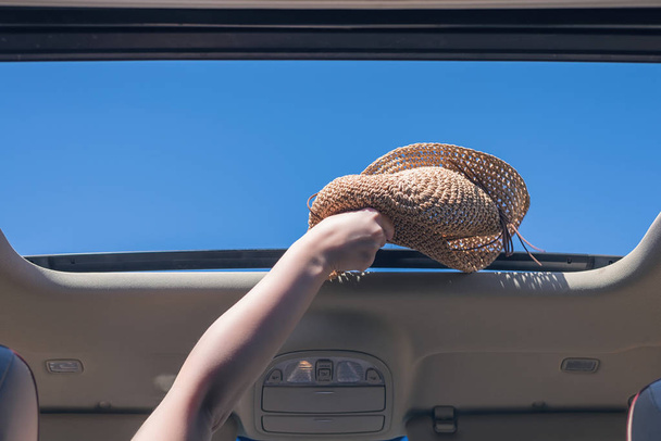 girl trowing away her straw hat out from open hatch of a vehicle. Travel lifestyle concept - Foto, imagen