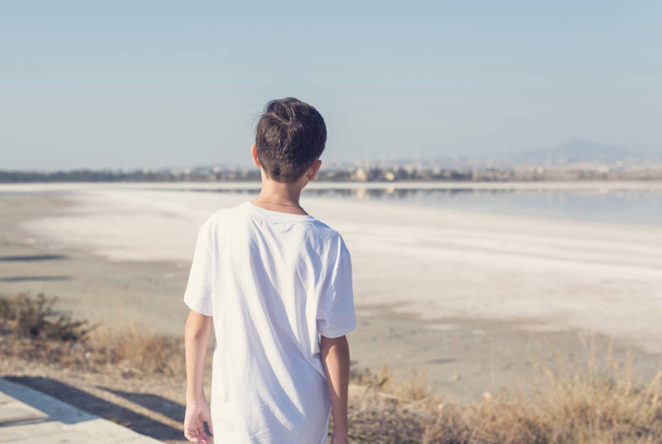 A boy in shorts and a T-shirt near the salt lake in Larnaca. Cyprus - Фото, изображение