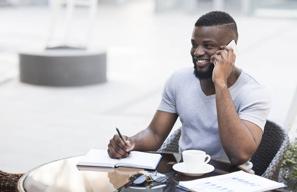 Χαμογελαστός Αφρικάνικος επιχειρηματίας με το σημειωματάριο στο καφέ - Φωτογραφία, εικόνα