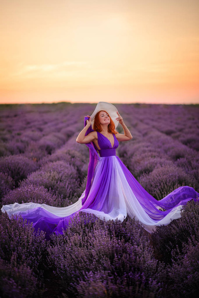 Happy red-haired woman in luxurious dress standing in lavender field at sunset - Valokuva, kuva