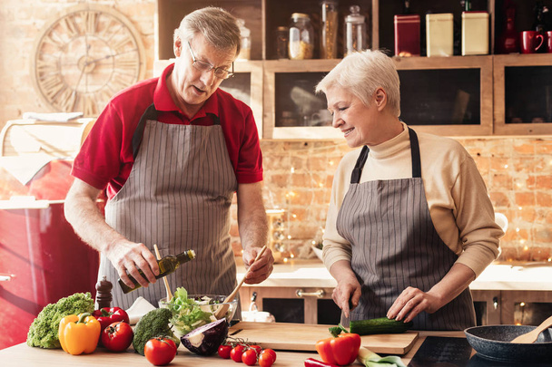 Senior liefdevolle paar het maken van gezonde salade samen in de keuken - Foto, afbeelding