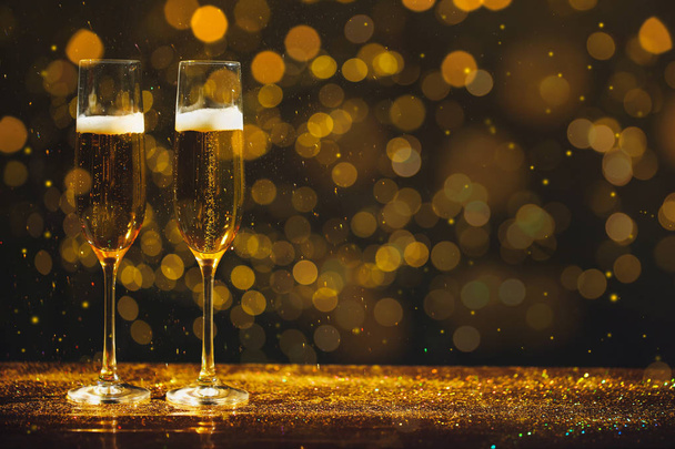 Glasses of champagne and golden glitter on table against blurred background, space for text. Bokeh effect - Photo, image