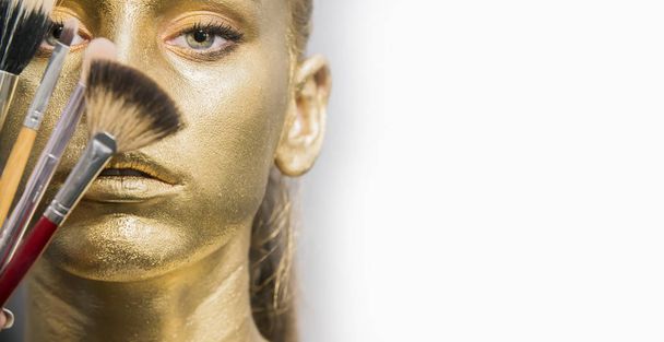 Close-up portret meisje houden make-up borstel, gouden gezicht make-up - Foto, afbeelding