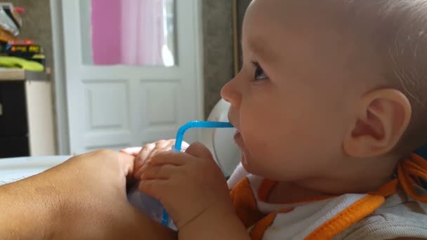 Lachende baby drinkt water via een plastic stro binnenshuis in de zomer in slowmotion - Video