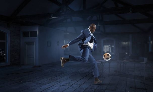 Black businessman plays football in a dark room - Foto, afbeelding