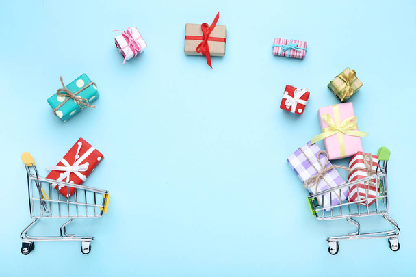 Small shopping carts with gift boxes on blue background - 写真・画像