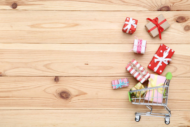 Small shopping cart with gift boxes on brown wooden table - Fotoğraf, Görsel