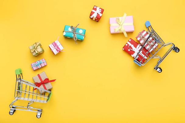 Small shopping carts with gift boxes on yellow background - Foto, Imagem