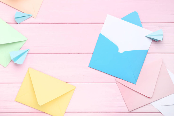 Colorful envelopes with paper planes on pink wooden table - Fotó, kép