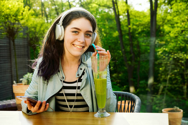 Νεαρή όμορφη γυναίκα που χρησιμοποιεί smartphone σε καφέ, πίνοντας χυμό σε γυαλί - Φωτογραφία, εικόνα