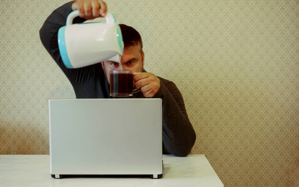 business man pouring coffee in cup on desk with laptop on wall background. young businessman - Foto, Imagem