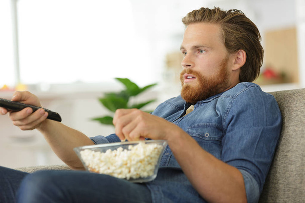 man eats pop-corn and watches tv - Фото, изображение