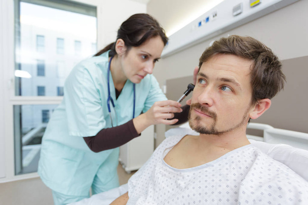 doctor examining patients inner ear in hospital bed - Φωτογραφία, εικόνα