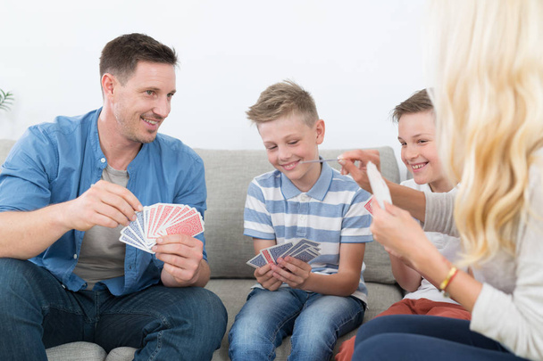 Szczęśliwa młoda rodzina gra w karty w domu. - Zdjęcie, obraz