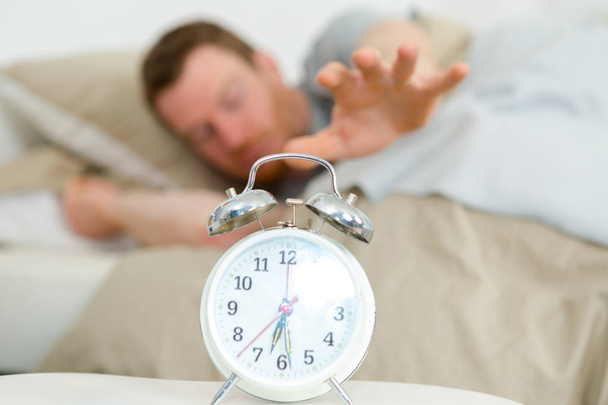 sleepy man reaching to snooze alarm clock - Fotografie, Obrázek