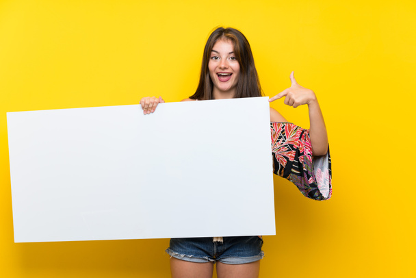 Izole sarı arka plan üzerinde renkli elbiseli Kafkas kız bir kavram eklemek için boş bir beyaz pankart tutarak - Fotoğraf, Görsel