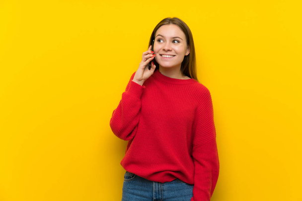 Mujer joven sobre pared amarilla manteniendo una conversación con el teléfono móvil
 - Foto, imagen