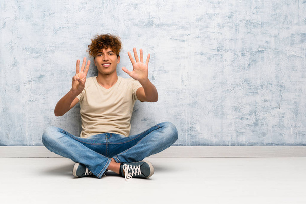 junger afrikanisch-amerikanischer Mann sitzt auf dem Boden und zählt mit den Fingern acht - Foto, Bild