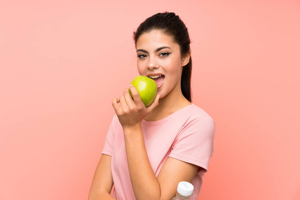 Dziewczyna Nastolatka na białym różowym ścianie z butelką wody i jabłkiem - Zdjęcie, obraz
